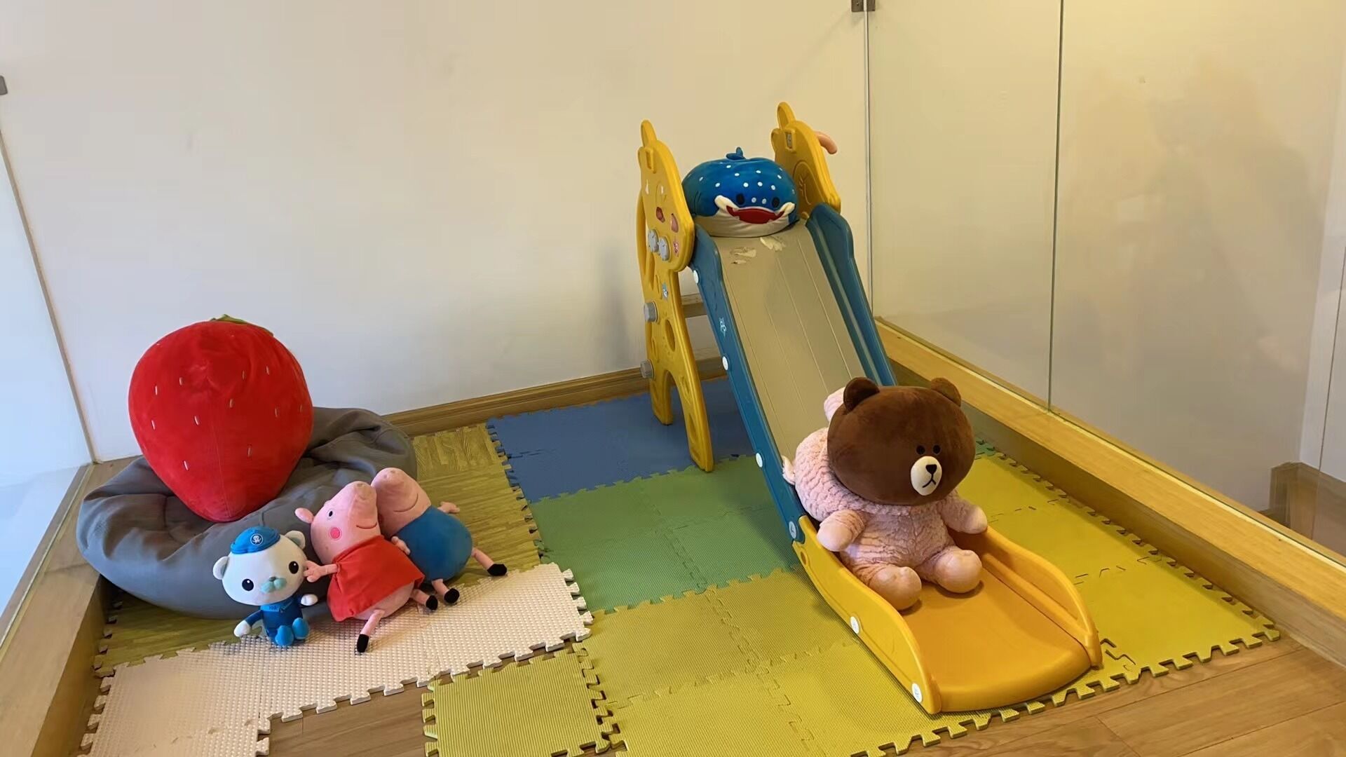 A play area with a slide, soft mats, and plush toys.