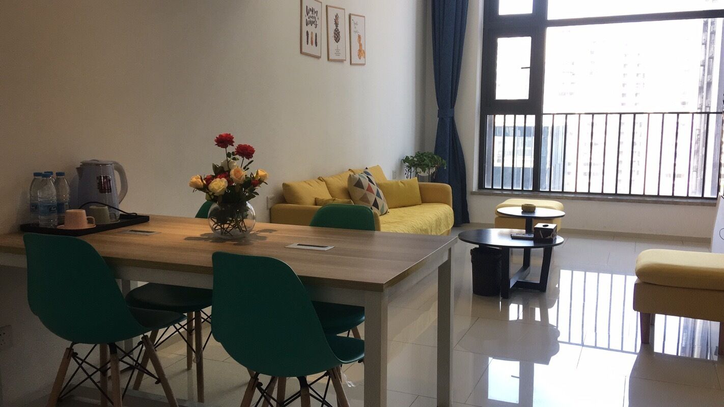 A modern living room with a wooden dining table, green chairs, a yellow sofa, and a small round table.