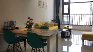 A modern living room with a wooden dining table, green chairs, a yellow sofa, and a small round table.