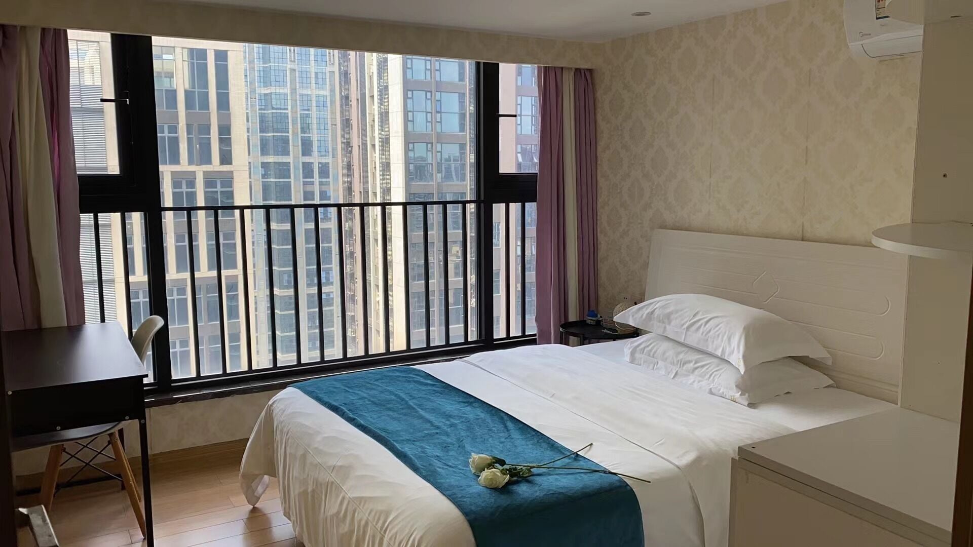 Una camera d'albergo con una grande finestra, un letto, una scrivania e una sedia.