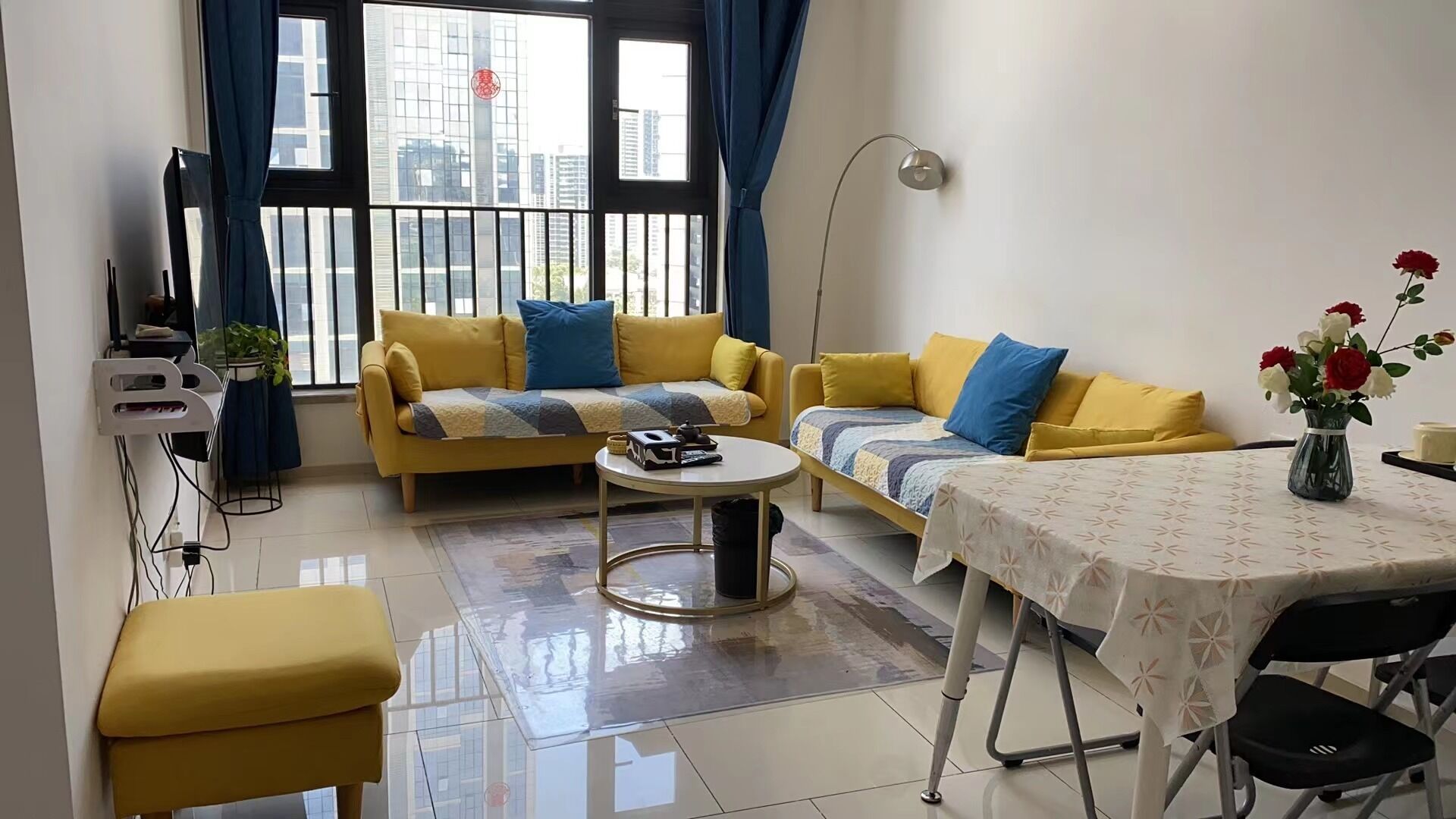 A modern living room with two yellow sofas, a coffee table, a dining table, and a TV.