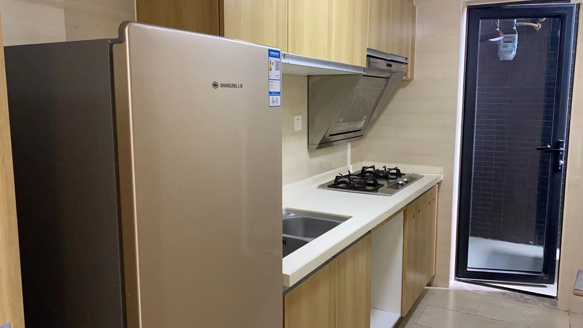 A compact kitchen with a stainless steel refrigerator, a gas stove, and wooden cabinets.