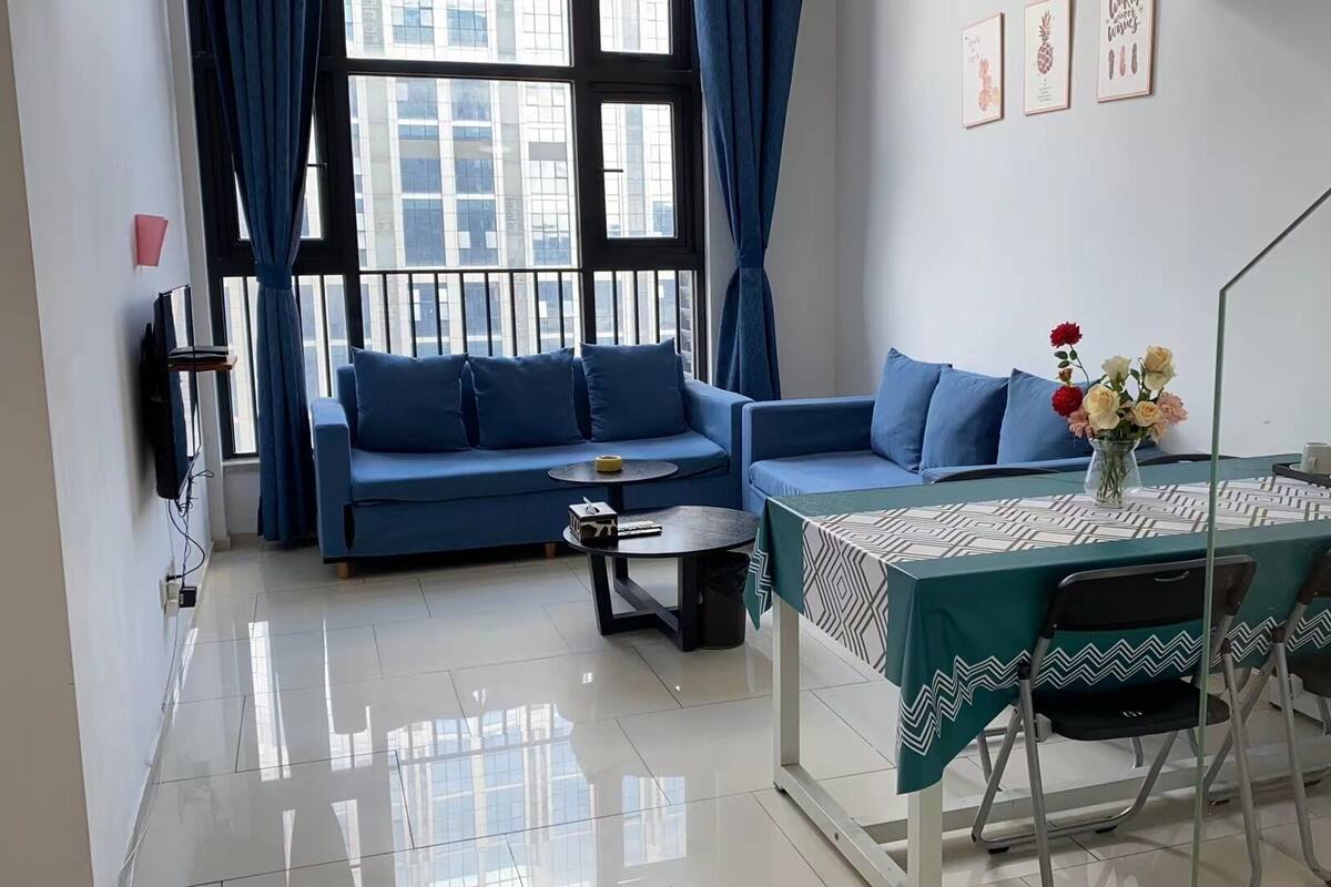 Un salon moderne avec un canapé bleu, une petite table ronde et un coin repas avec une table mise pour deux personnes.