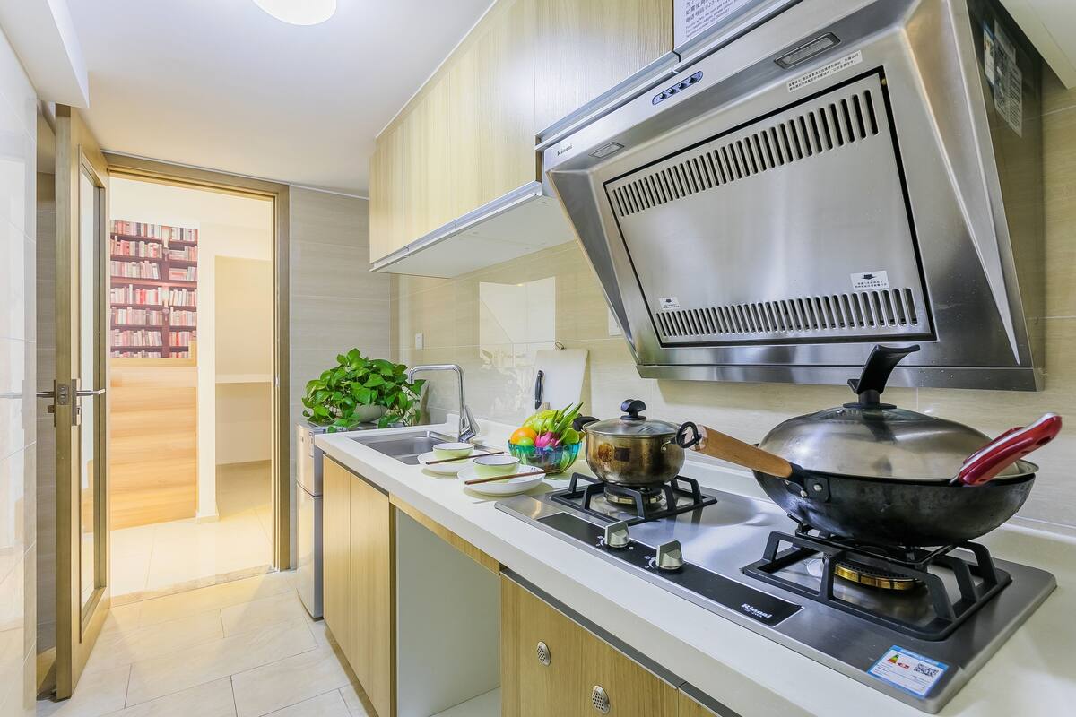 Une cuisine moderne équipée d’une cuisinière à gaz, d’appareils électroménagers en acier inoxydable et de meubles de rangement en bois.