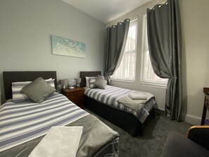 Una habitación de hotel con dos camas individuales, una mesita de noche con lámpara, una pequeña mesa y una silla.