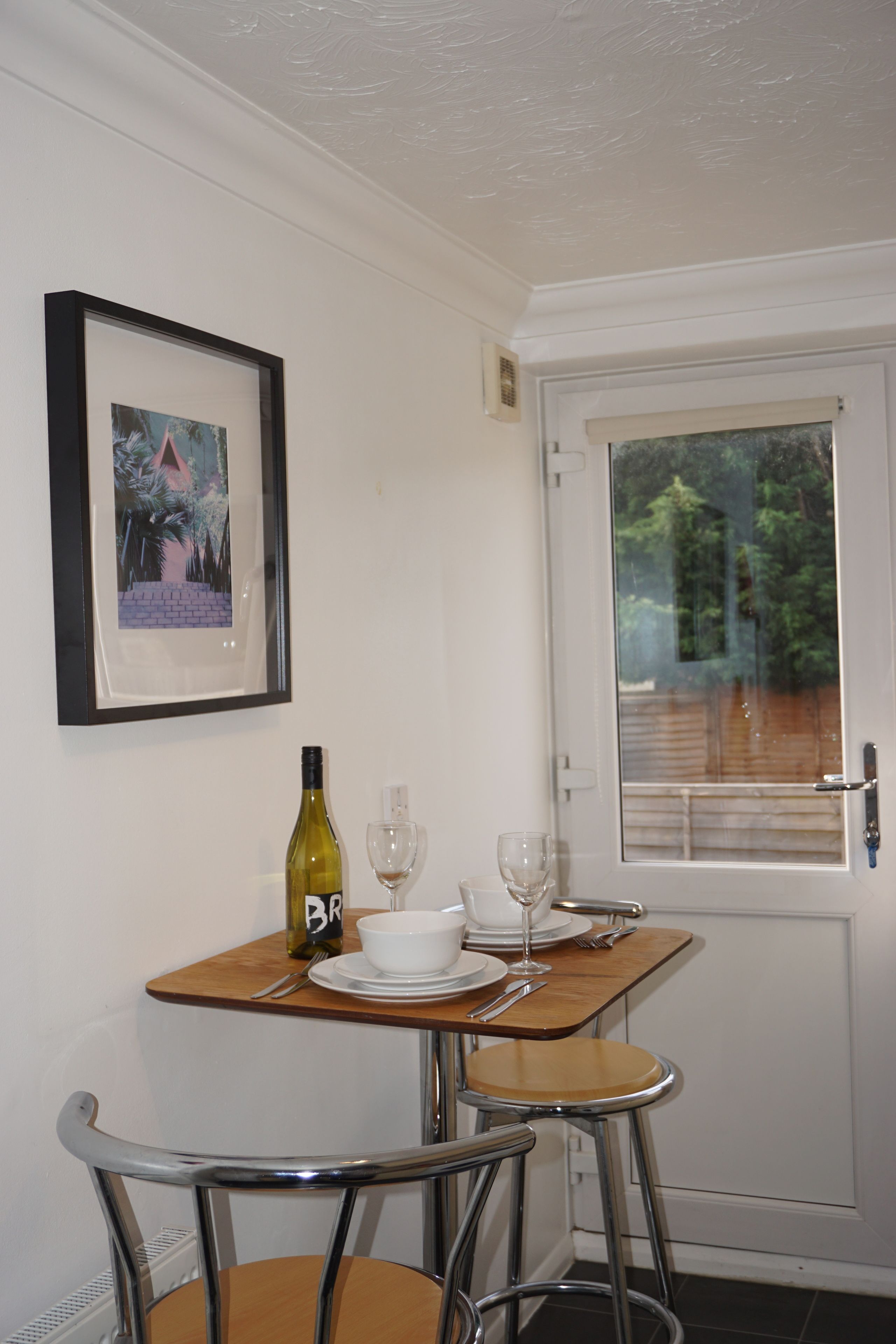 A small dining area with a table, chairs, a wine bottle, and a framed picture on the wall.