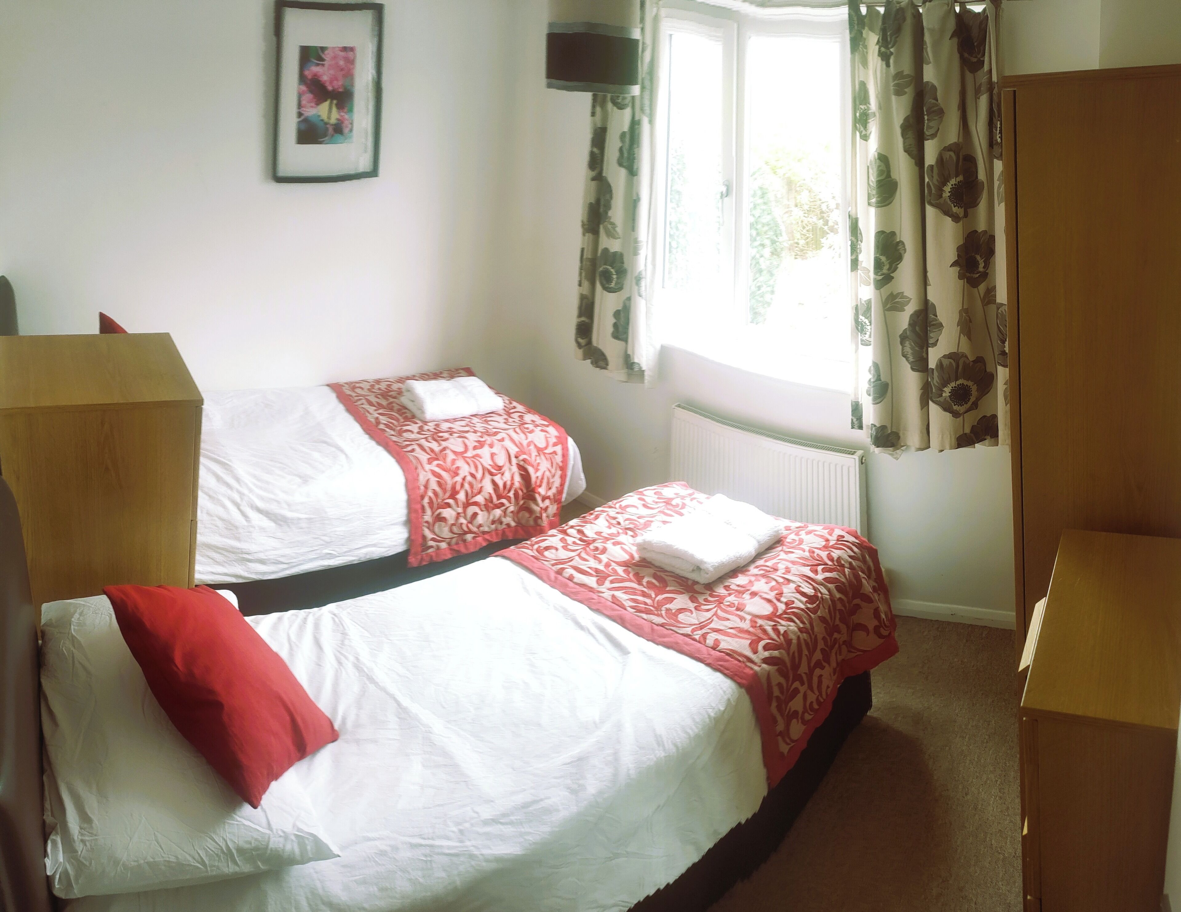 Une chambre avec deux lits, un radiateur, une fenêtre avec des rideaux et une armoire en bois.