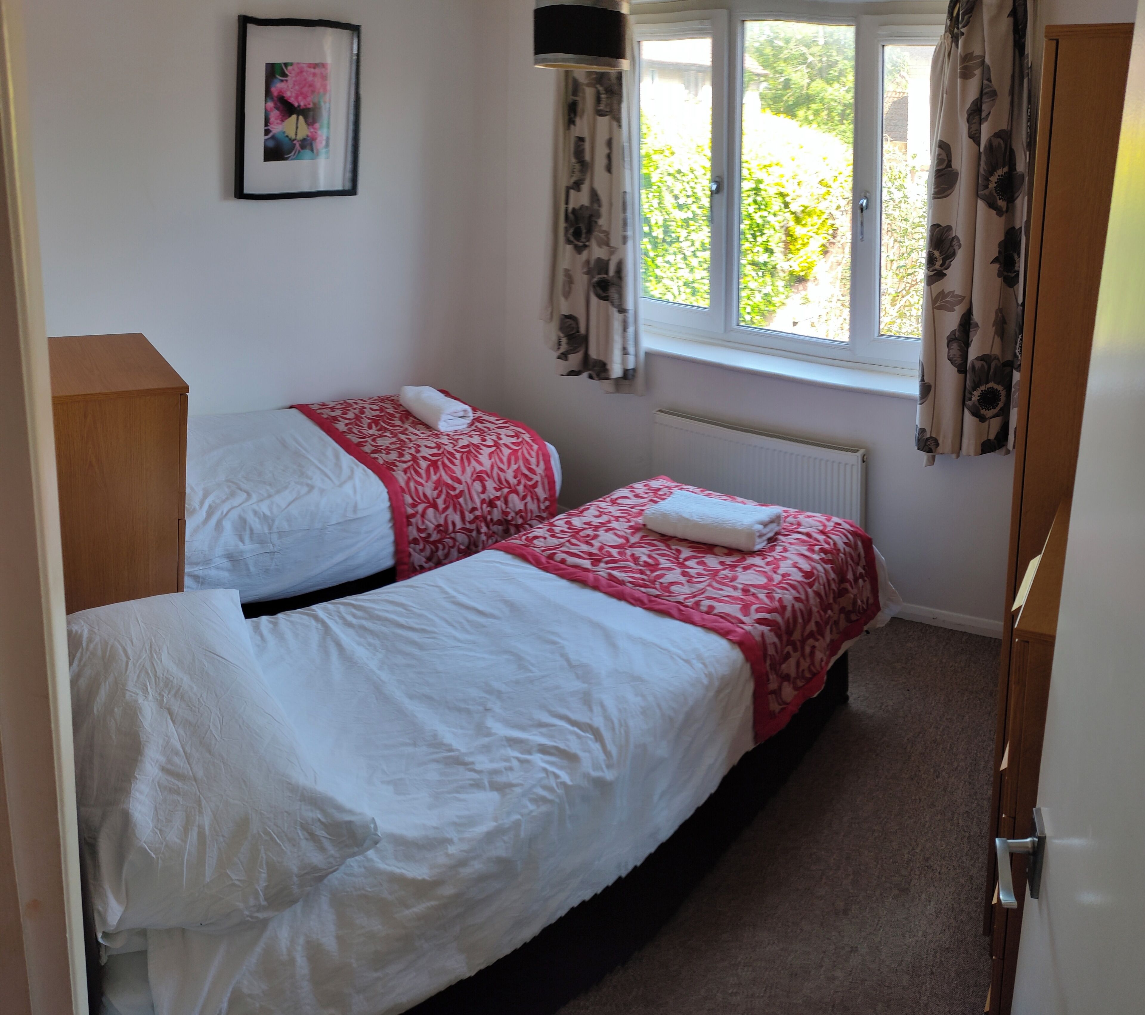 A bedroom with two single beds, a radiator, a window with curtains, and a door.