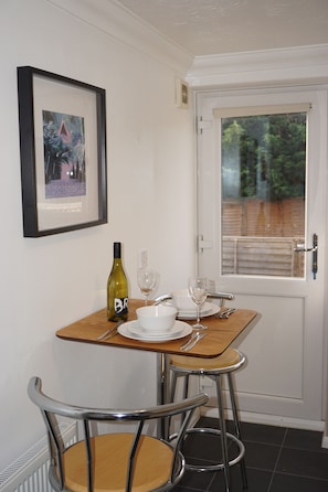 A small dining area with a table set for two, a bottle of wine, and a framed picture on the wall. - Holt Apartment (Bristol)