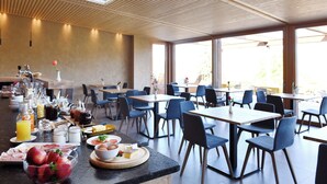 A modern dining area with a long breakfast bar, blue chairs, and large windows. - Bad St.Isidor (Bolzano)