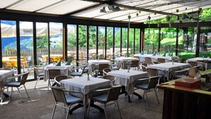 An outdoor dining area with tables and chairs, large windows, and a view of a garden. - Bad St.Isidor (Bolzano)