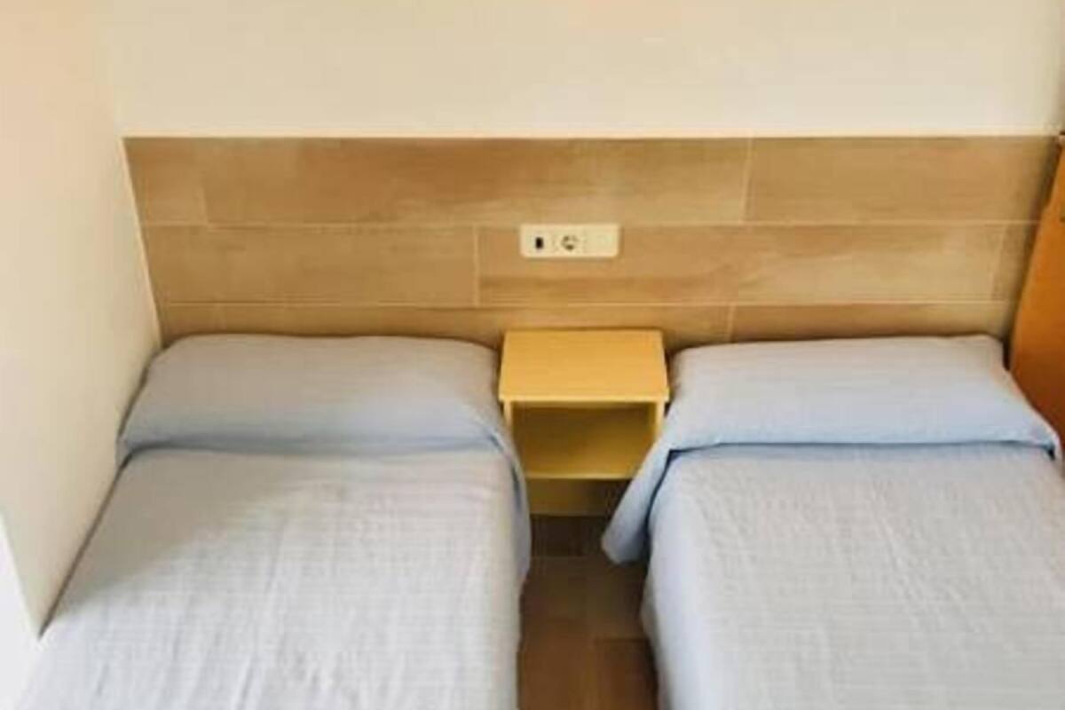 Habitación doble con dos camas individuales, cabecero de madera, mesita de noche y lámpara de pared.