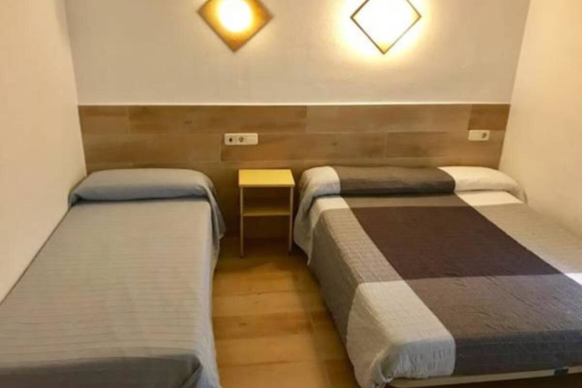 Una habitación con dos camas individuales, una mesita de noche pequeña y dos lámparas fijadas a la pared.