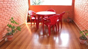 A small, enclosed patio area with a brick wall, a wooden floor, a round table, and red plastic chairs. There are potted plants on the floor. - Hotel Lake Valley (Pokhara)