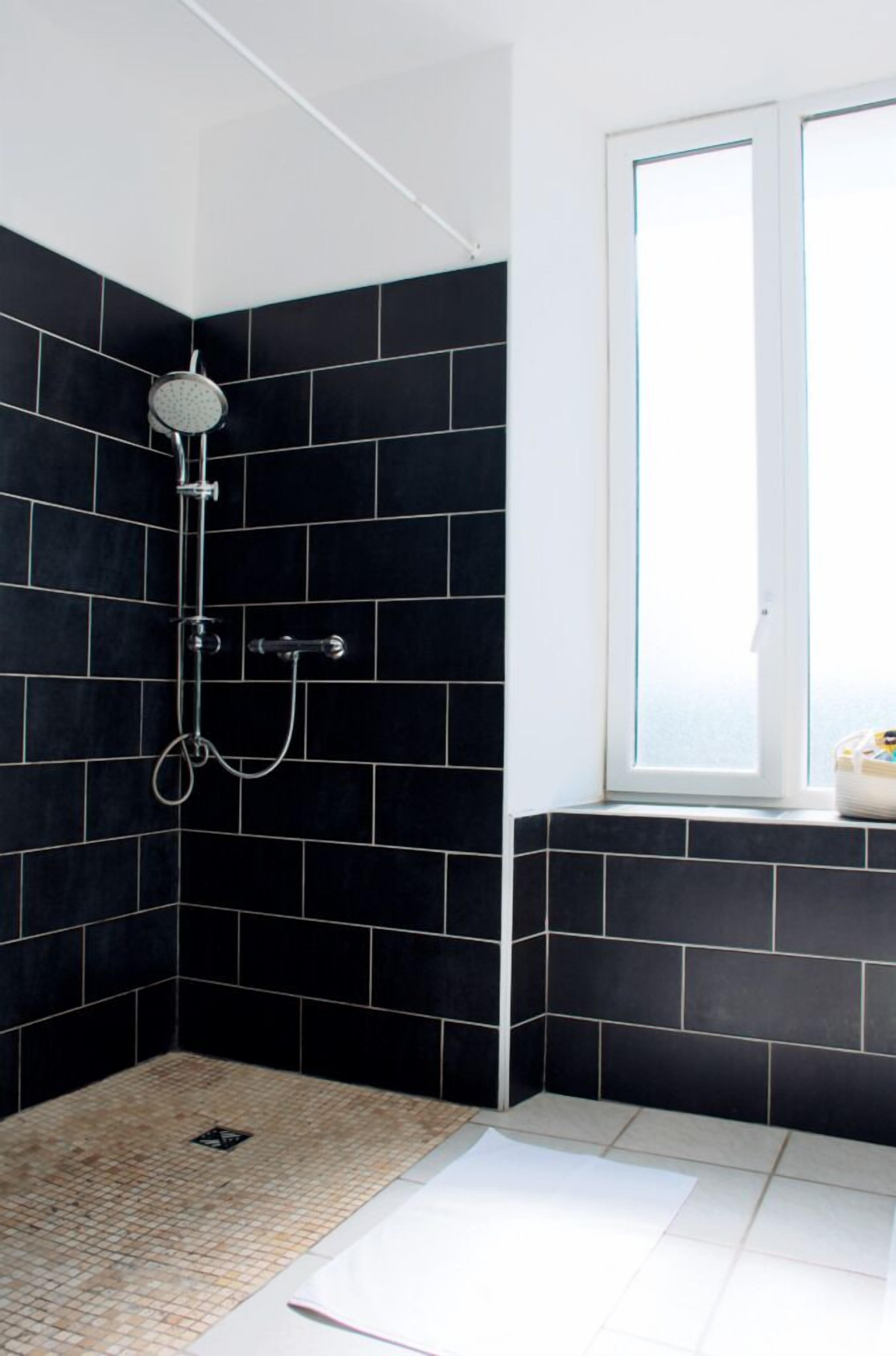 A shower area with black tiles, a window, and a white door.