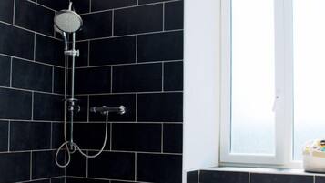 A shower area with black tiles, a window, and a white door.