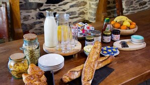 A breakfast buffet with bread, pastries, fruits, and dairy products on a wooden table. - Valfrescos (Caurel)