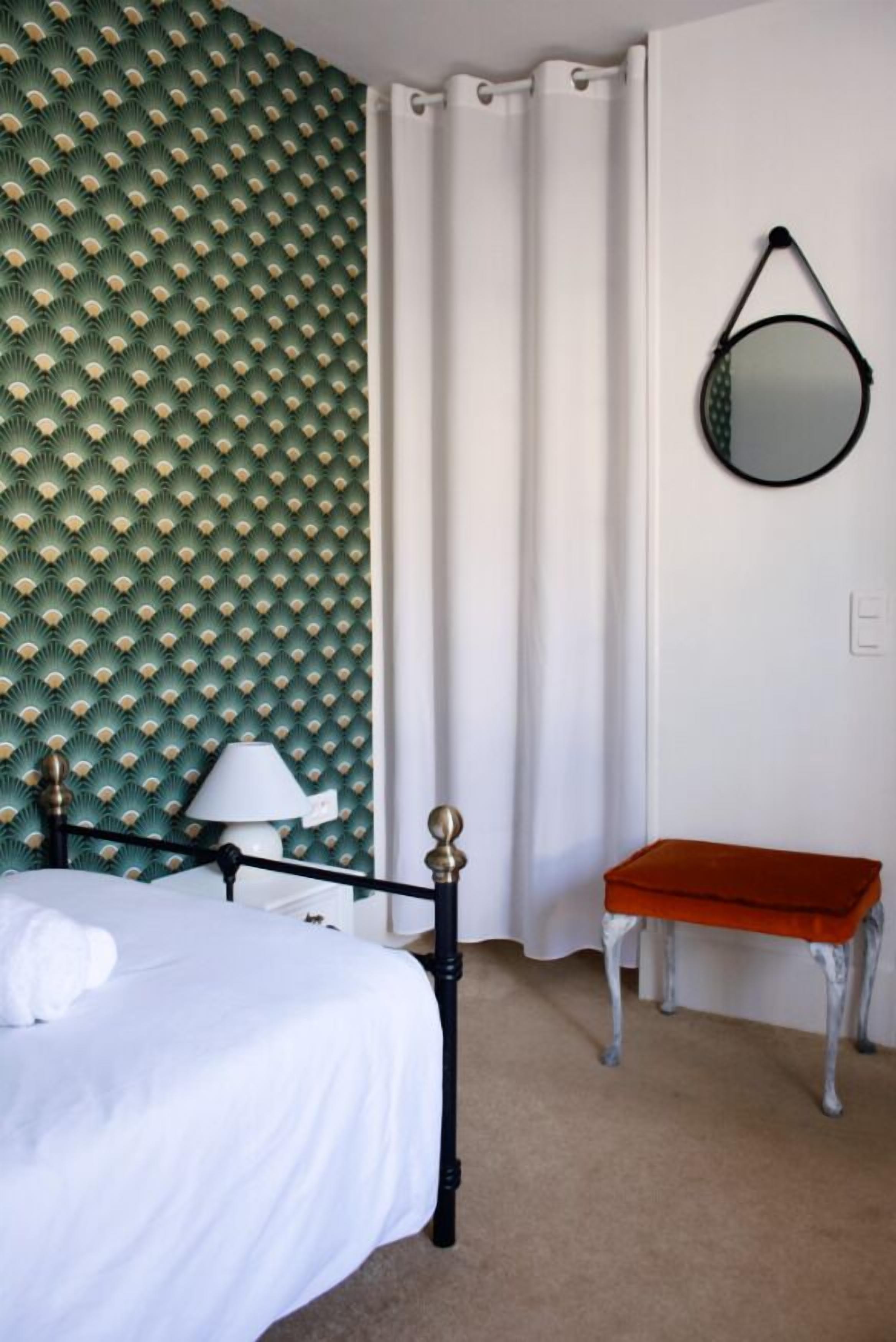 Ein Schlafzimmer mit einem Bett, einem Nachttisch, einer Lampe, einem Spiegel und einer roten Bank.
