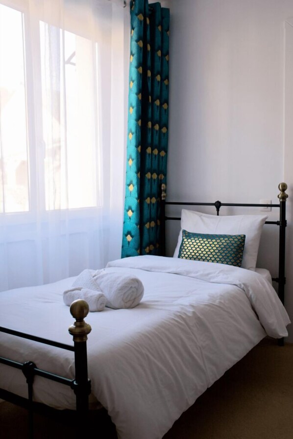 A neatly made bed with white linens, a teal patterned pillow, and a white towel on the side. - Valfrescos (Caurel)