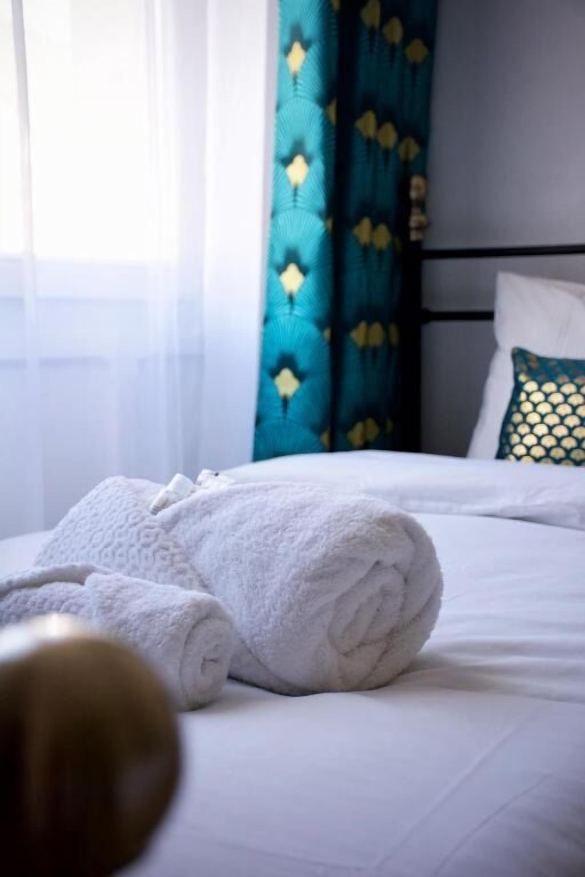 Un lit bien fait, avec du linge de lit blanc et une serviette blanche enroulée posée sur le côté.