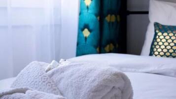 Un lit bien fait, avec du linge de lit blanc et une serviette blanche enroulée posée sur le côté.