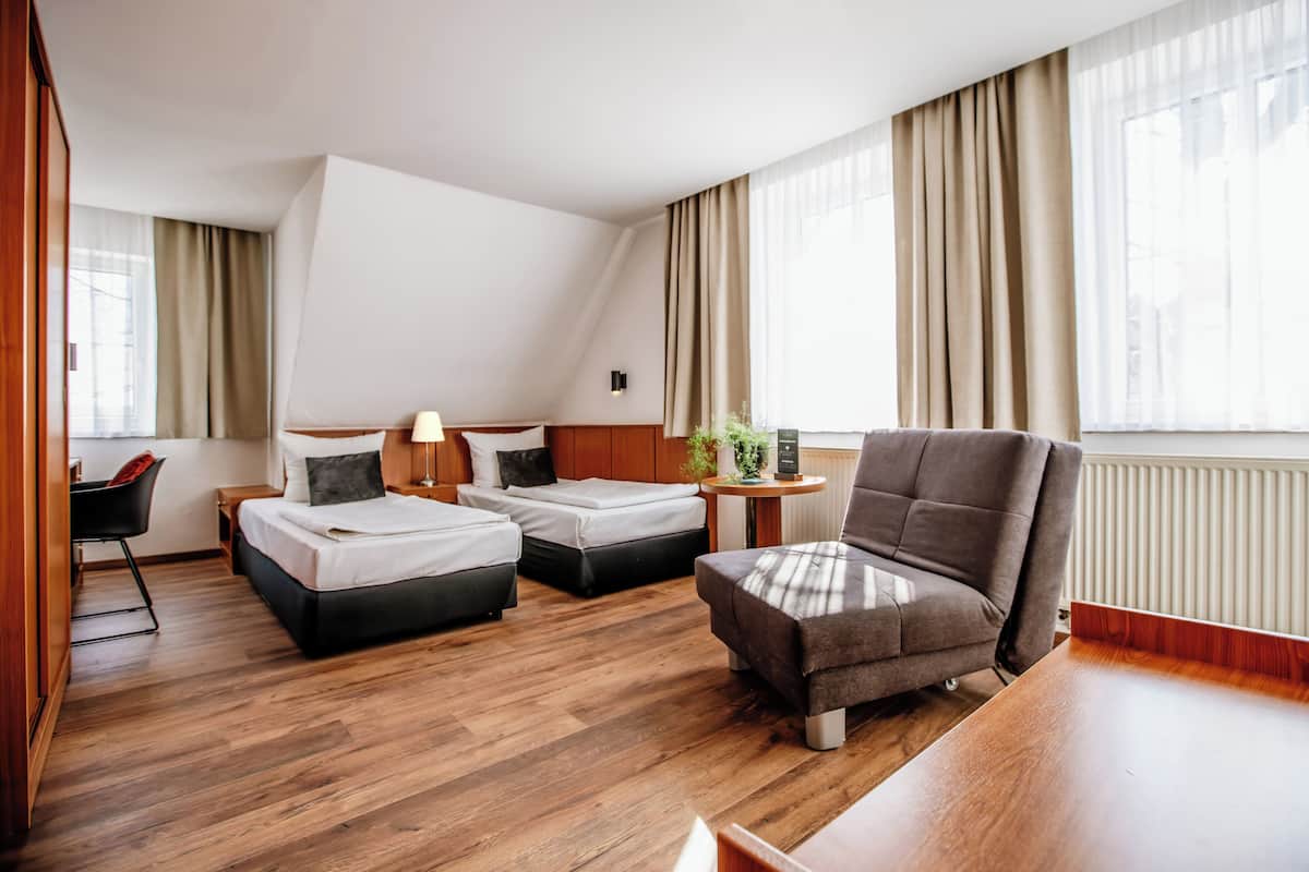A hotel room with two beds, a sofa, a desk, and a chair.