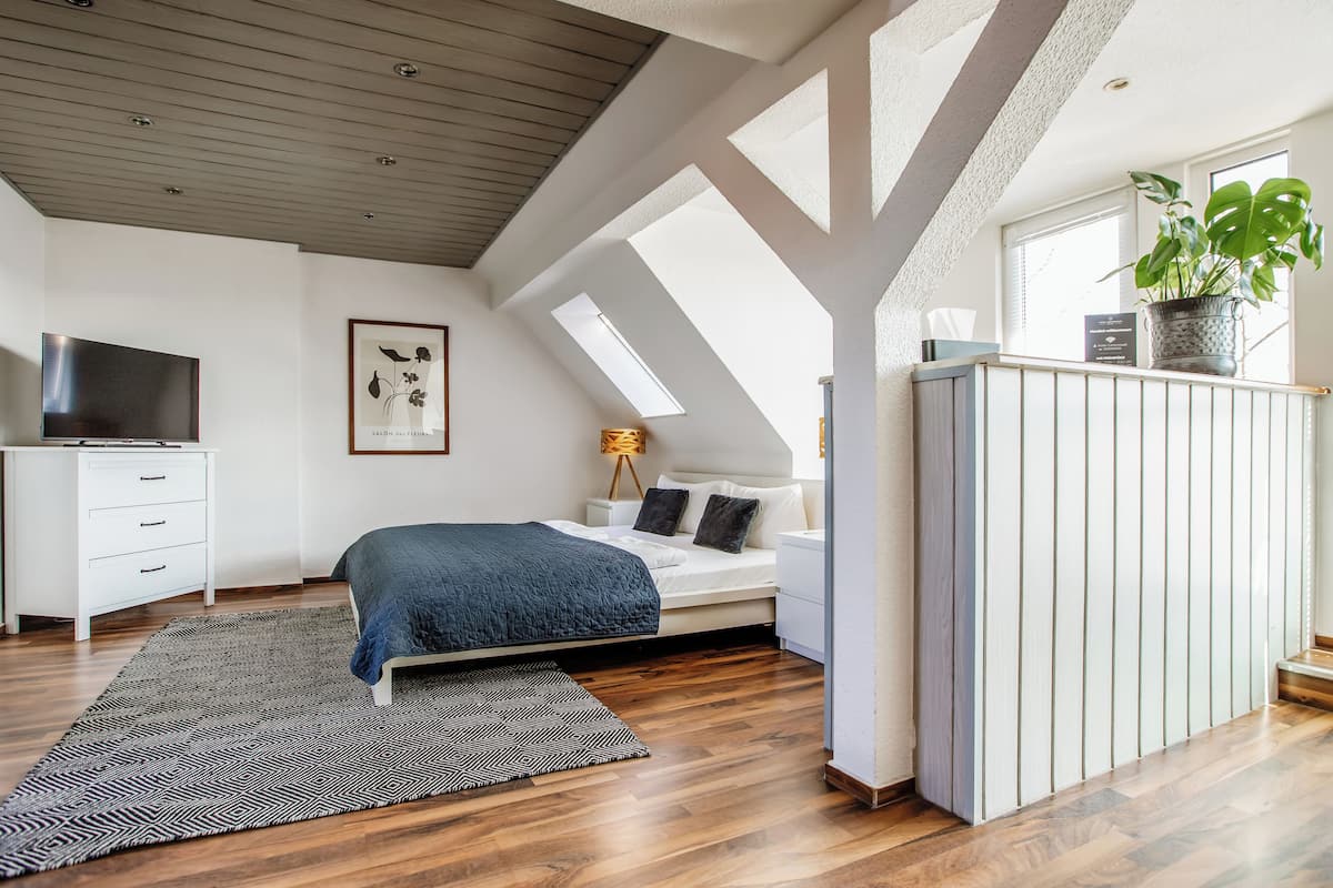 A bedroom with a bed, a desk, a TV, and a potted plant.