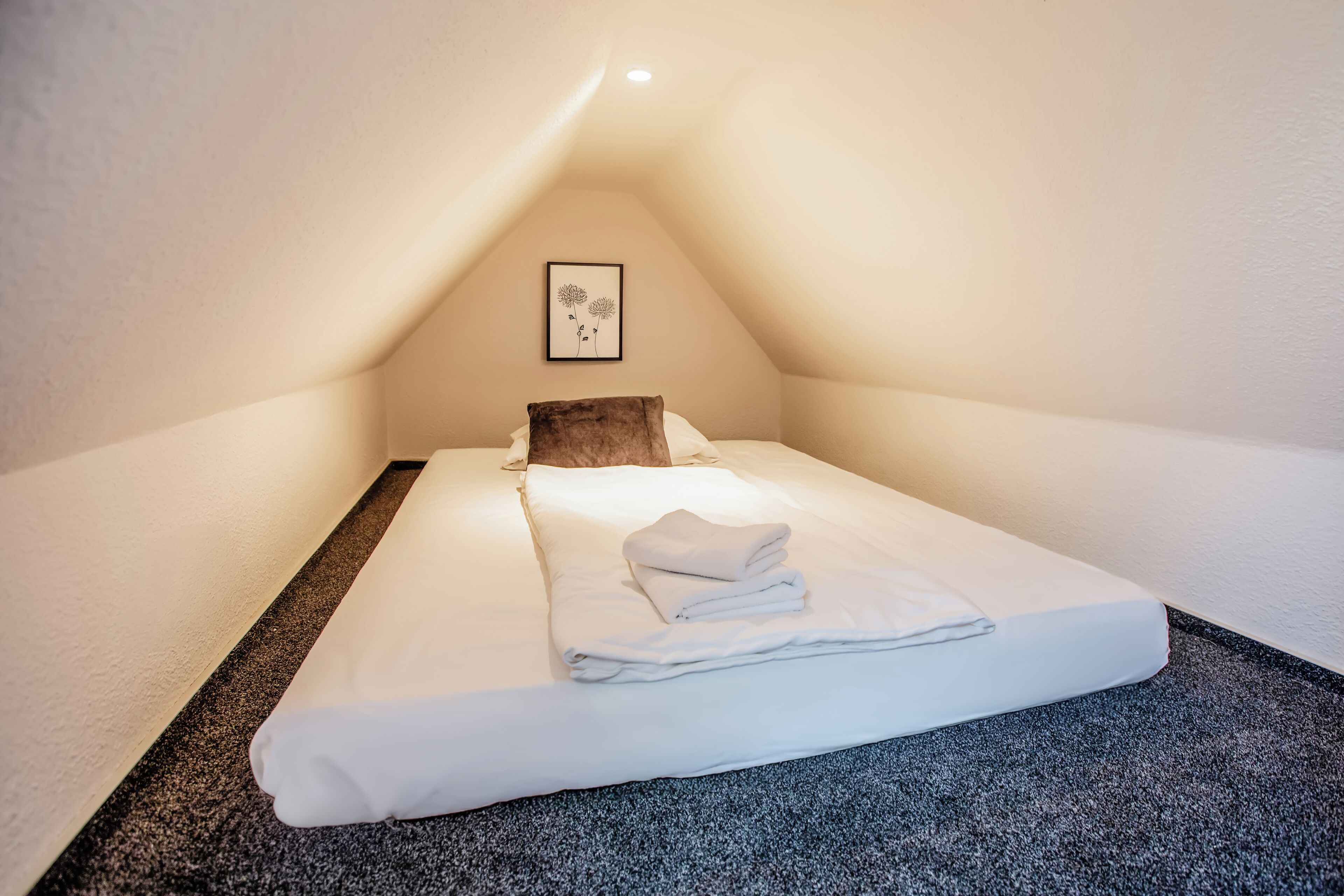 Un lit bien fait dans une petite pièce triangulaire, avec un seul tableau encadré accroché au mur.
