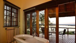 Un baño con bañera, persianas de madera y vistas a una terraza con mobiliario exterior.