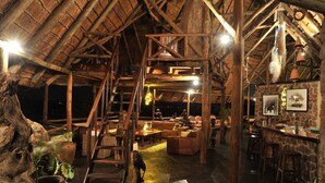 Un interior con techo de madera rústica, pared de piedra con cuadros y una zona de bar.