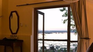 Un dormitorio con una cama grande, una ventana con cortinas y vistas a un cuerpo de agua.