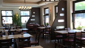 En restaurant med flere borde og stole, en lysekrone og store vinduer.