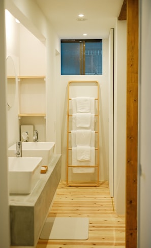 A narrow bathroom with a wooden floor, a window, and a towel rack with multiple towels.
