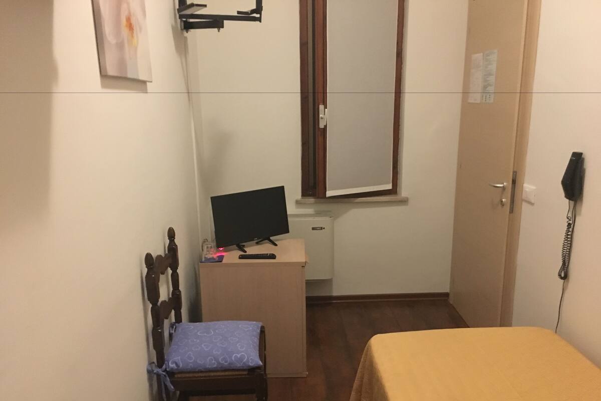 A small room with a desk, a chair, a bed, a mirror, and a telephone.