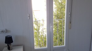 Una habitación con una puerta blanca, una pequeña mesa blanca con una lámpara, y vistas a zonas verdes al exterior.