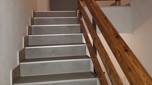 Una escalera con barandillas de madera y escalones grises que conducen a una puerta.