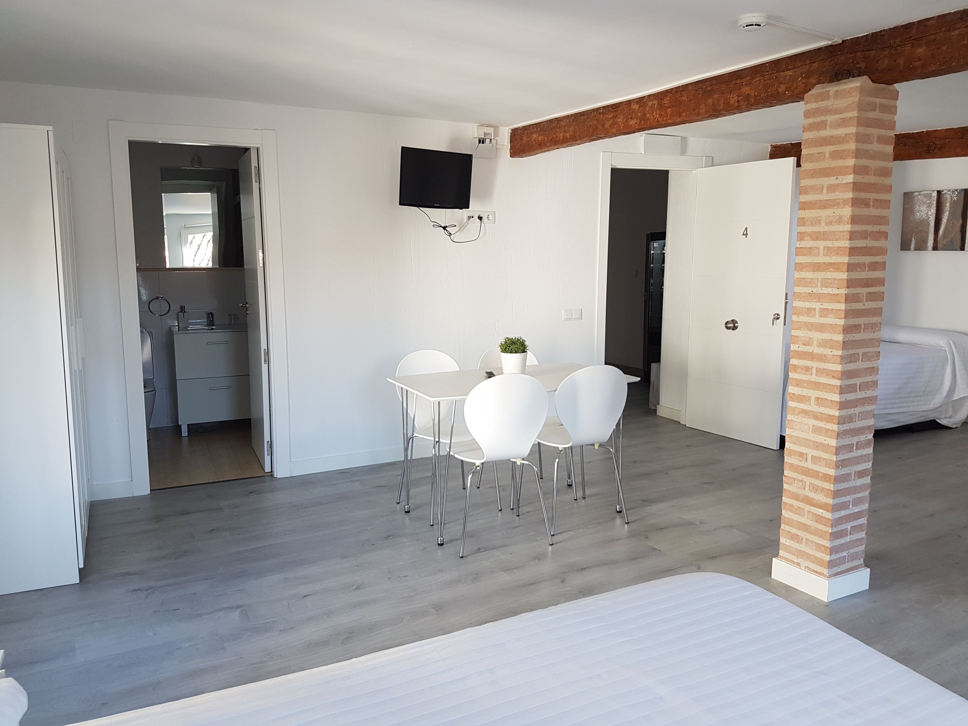 A modern room with a dining area, a TV mounted on the wall, and a brick column.