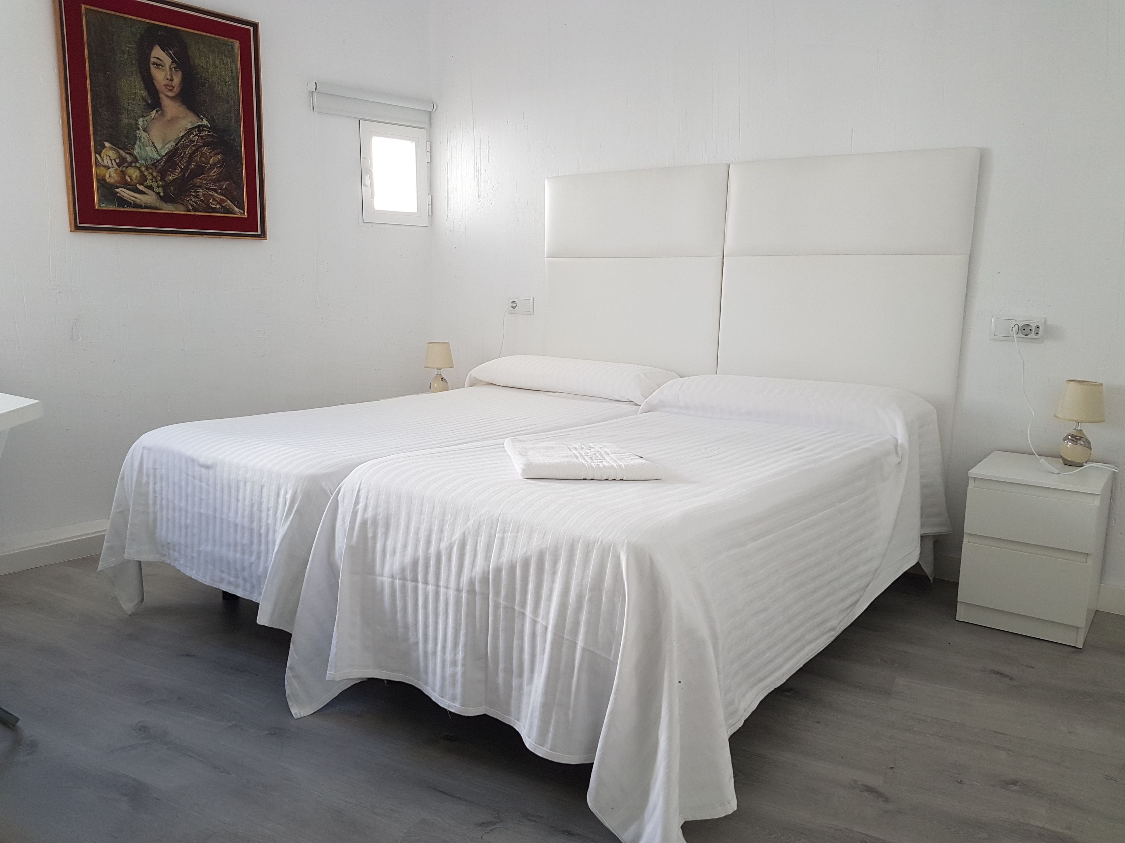 A bedroom with a large bed, two bedside tables, a nightstand, a window, and a painting on the wall.