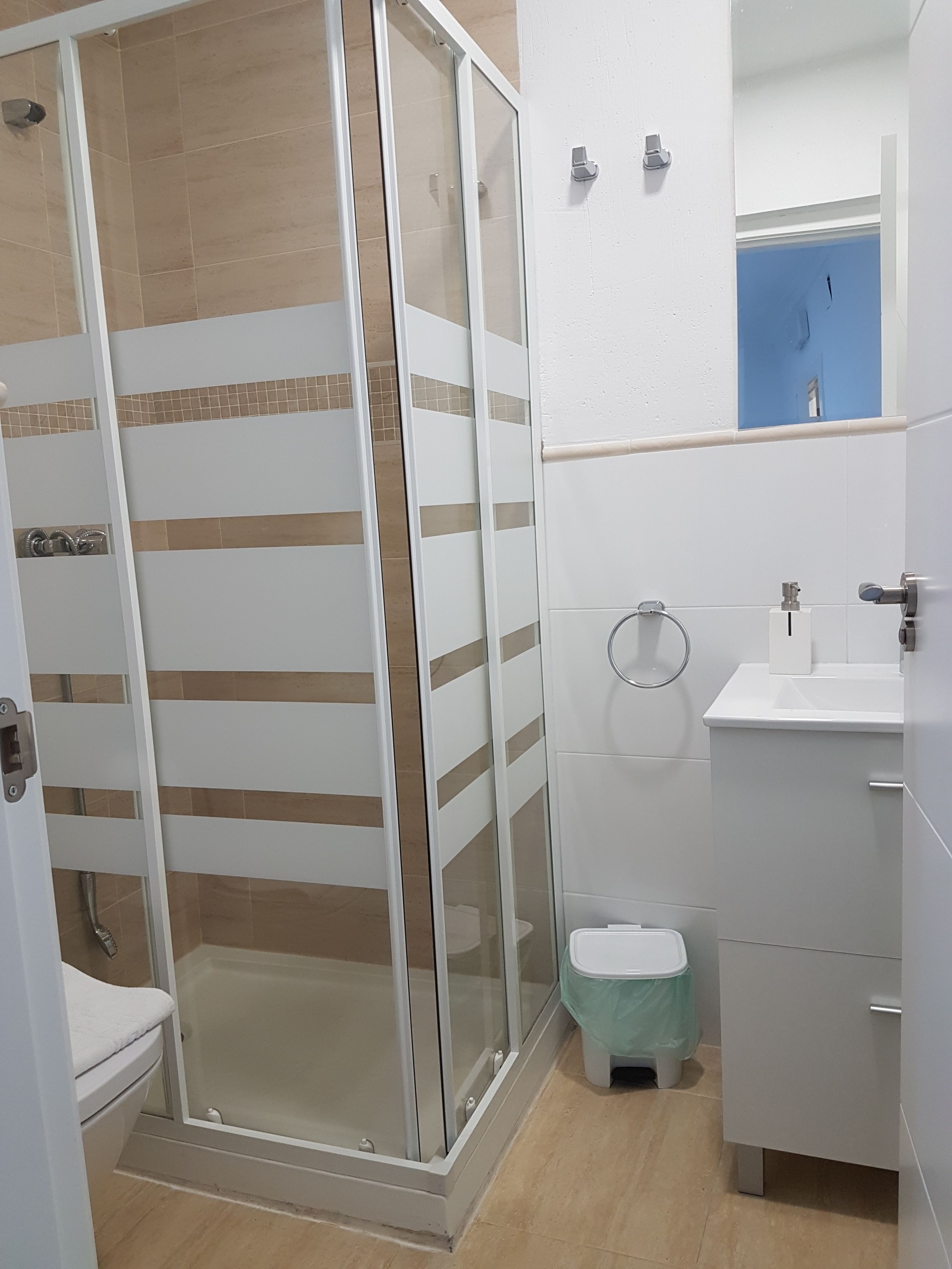 Ein Badezimmer mit Duschkabine aus Glas, Toilette, Waschbecken und Spiegel.