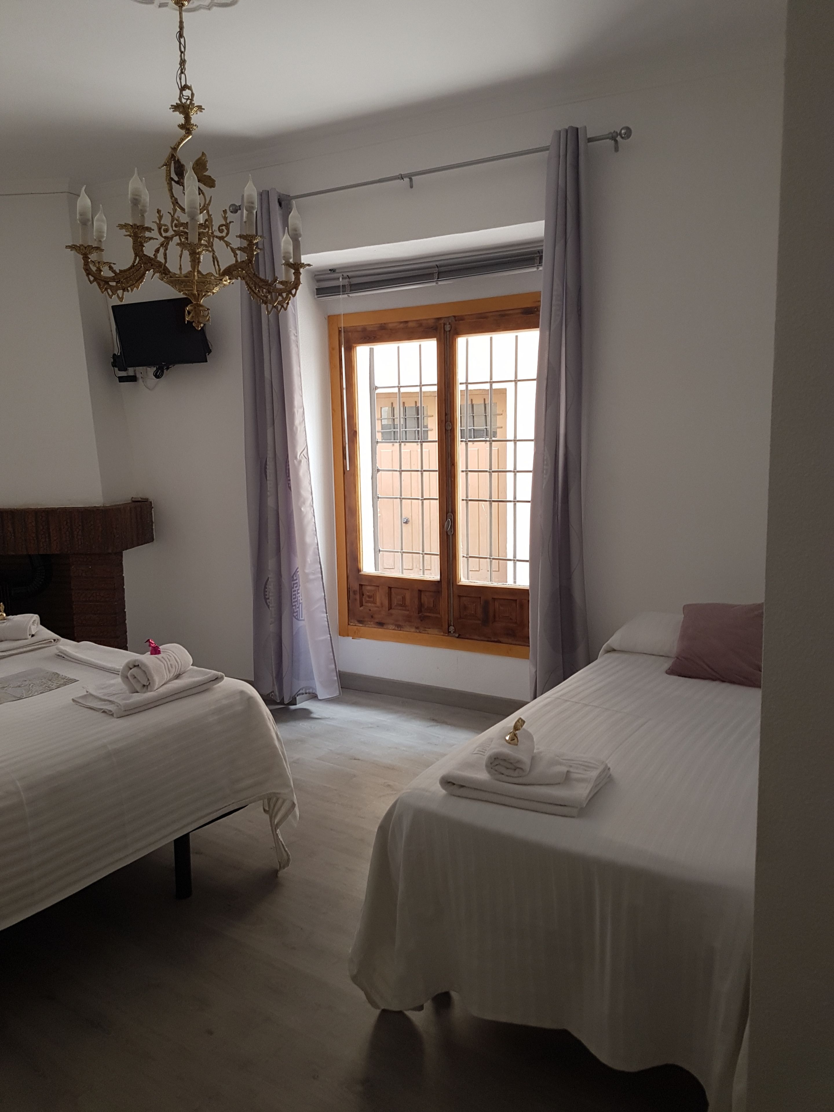 Une chambre d’hôtel avec deux lits, un lustre, une fenêtre avec des rideaux et une porte en bois.