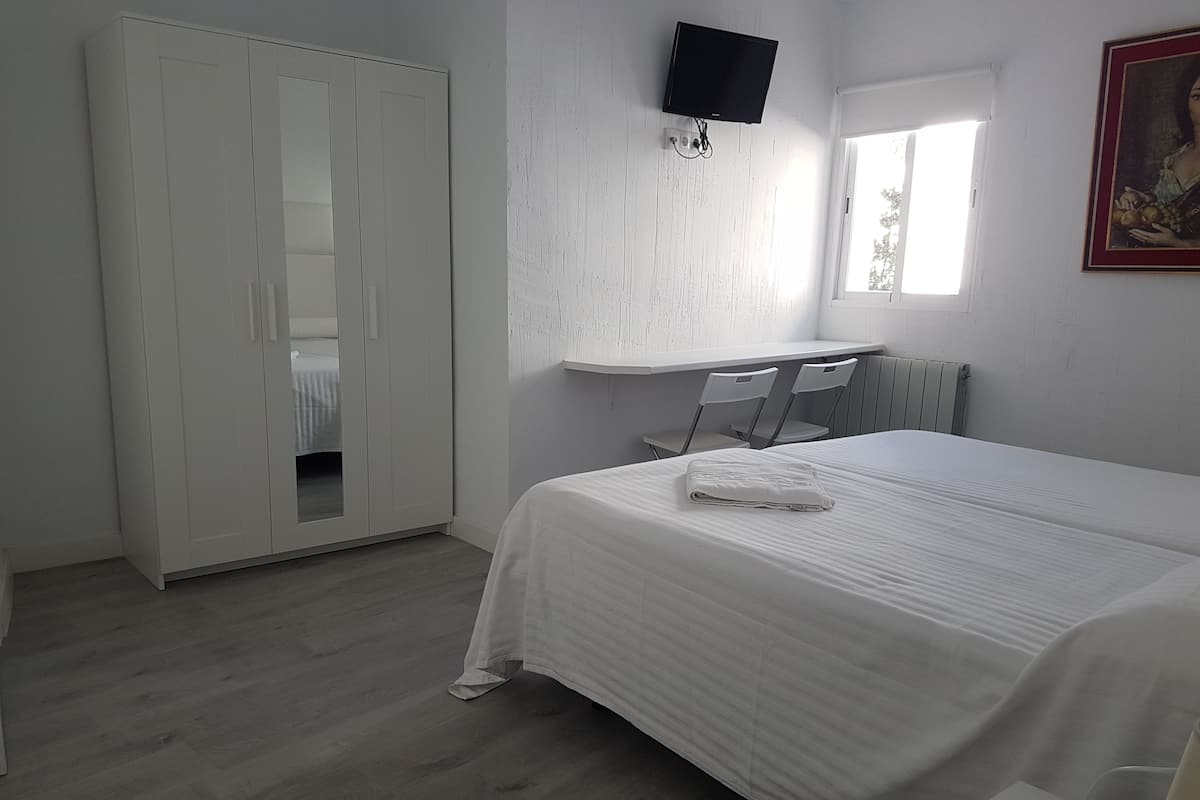 A bedroom with a bed, a wardrobe, a desk, a chair, a radiator, and a TV mounted on the wall.