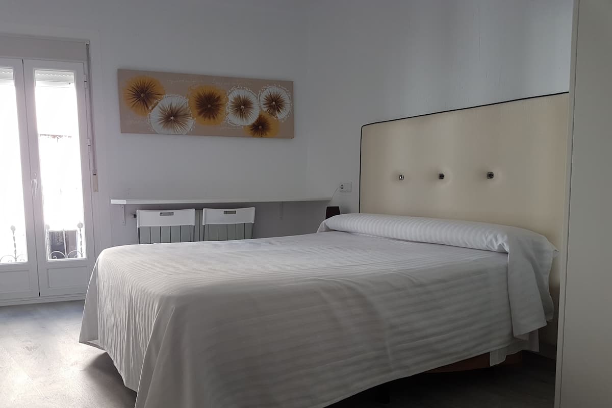 A bedroom with a bed, a desk, and a window.