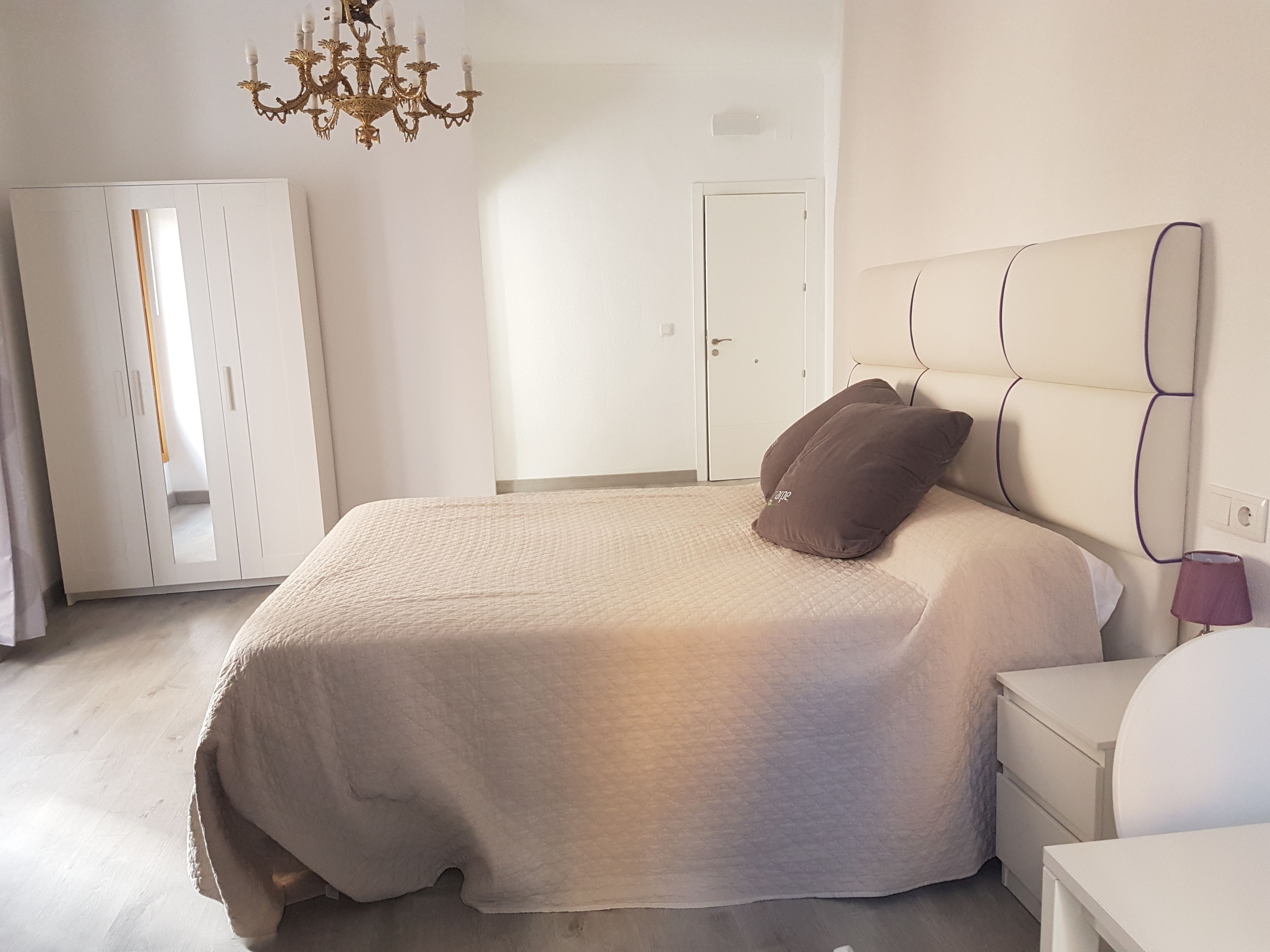 A bedroom with a bed, a nightstand, a dresser, a wardrobe, and a chandelier.