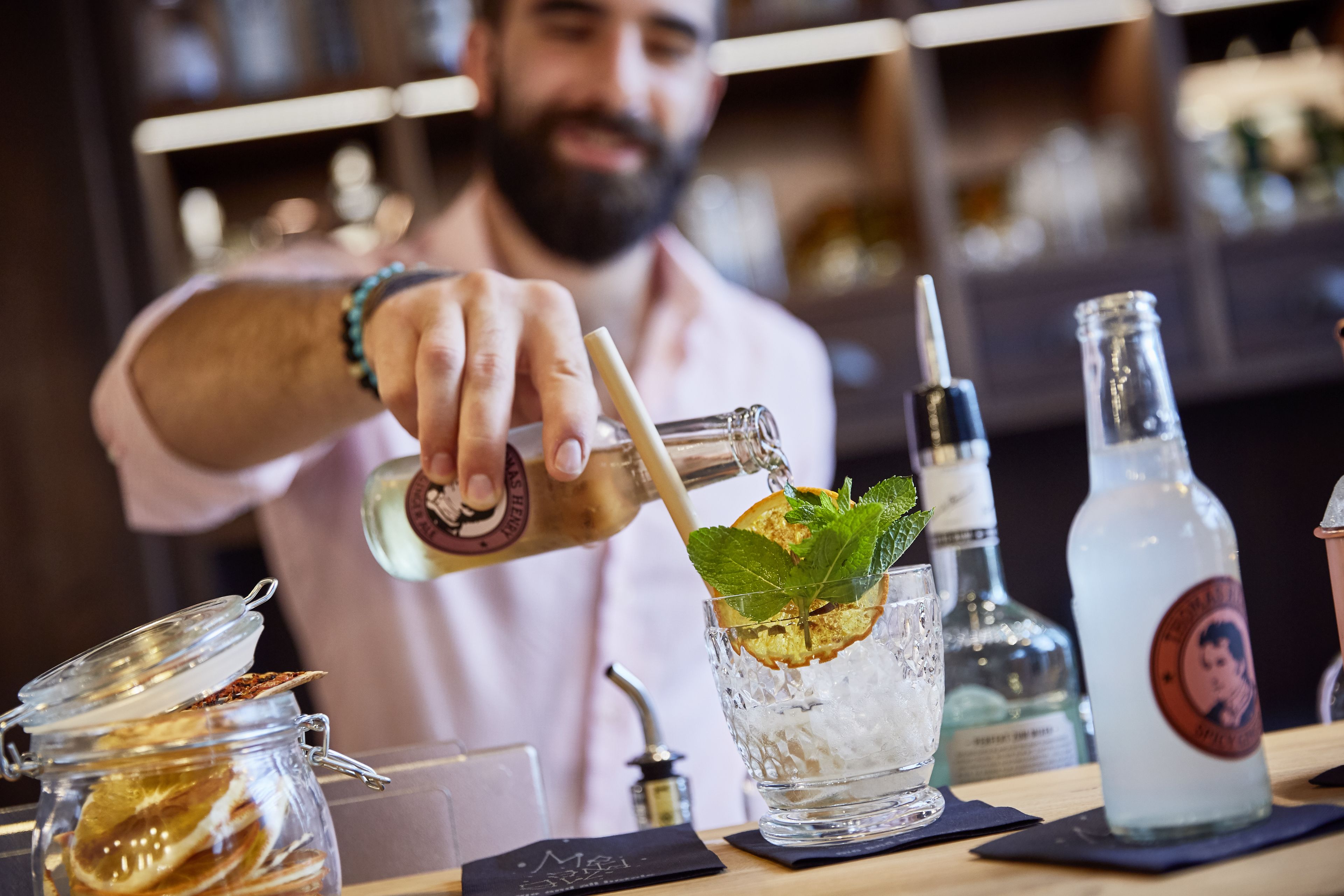 Un barman verse une boisson dans un verre rempli de glaçons et décoré d’une feuille de menthe.