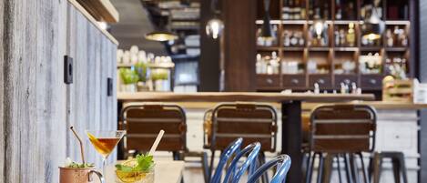 A bar area with a wooden wall, blue chairs, and a bar counter with shelves in the background.