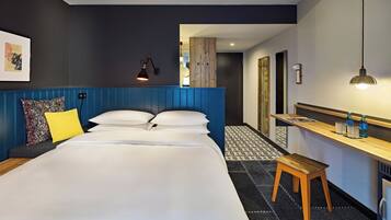 A hotel room with a large bed, a wooden bench, a desk with a mirror, and a patterned floor.