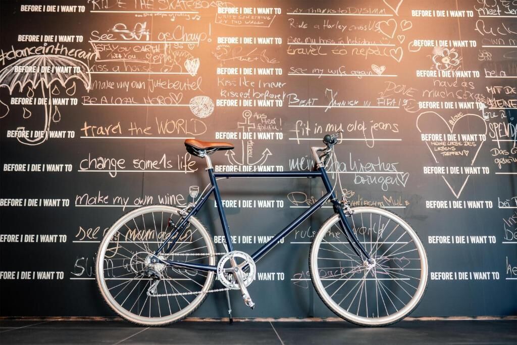 A bicycle with a black frame and white wheels, leaning against a wall with various handwritten notes and phrases.