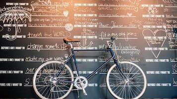 A bicycle with a black frame and white wheels, leaning against a wall with various handwritten notes and phrases.