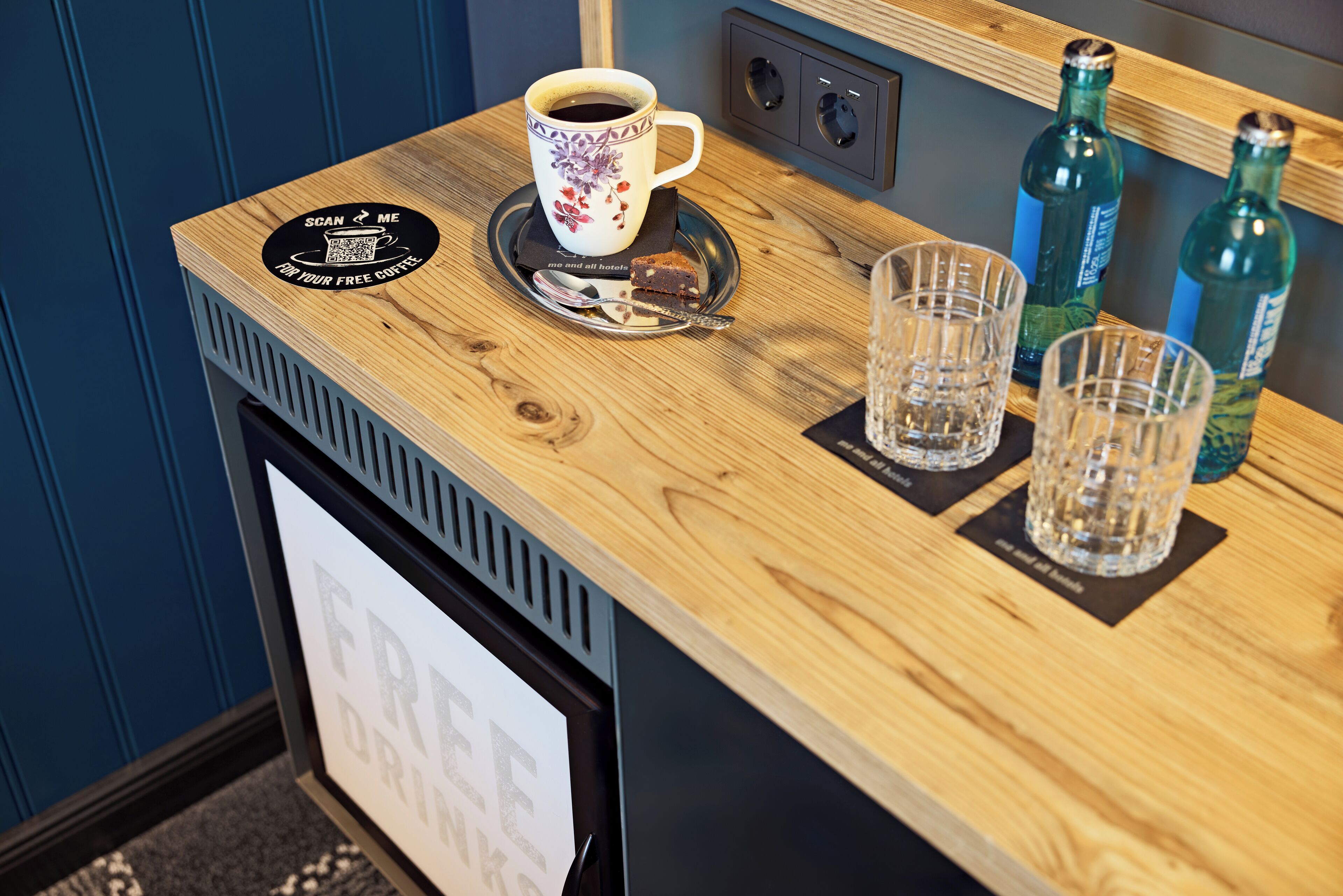 Una encimera de madera con una taza de café, dos vasos y dos botellas.