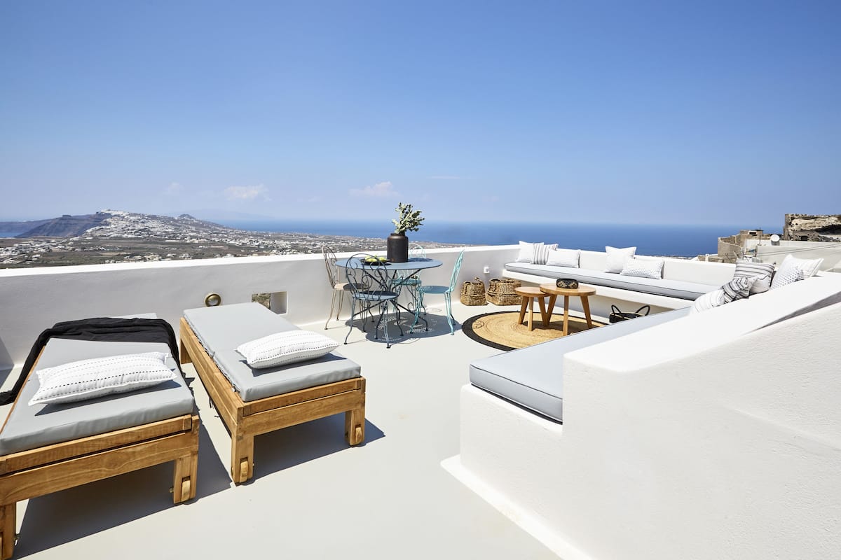 A rooftop terrace with lounge chairs, a table, and a view of the sea and cityscape.